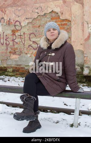 Das Mädchen saß im Winter auf der alten Straße auf dem Metallgeländer Stockfoto