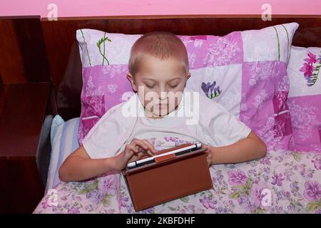 Junge im Schlafzimmer auf dem Bett spielen Spiele auf dem Tablet Stockfoto