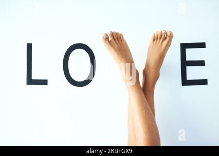 Wandelt auf dem Pfad der Liebe. Studioaufnahme eines nicht erkennbaren mannes kreuzte die Beine, wobei seine Füße den Buchstaben V im Wort LIEBE bildeten. Stockfoto