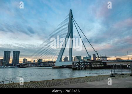 Erasmusbrug oder die Erasmus-Brücke, wie sie am 20. Januar 2020 in einer magischen Stunde am Winterabend mit buntem Himmel im Stadtzentrum der niederländischen Stadt Rotterdam, Niederlande, zu sehen ist. Die 802m. Lange Brücke über das Wasser der Neuen Maas ist eine von Ben van Berkel entworfene, nach Desiderius Erasmus benannte Brücke mit Kabelgestellen und Bascule. Die Konstruktion und die Struktur sind berühmt für ihre moderne Architektur und das asymmetrische, blassblaue Pylondesign, das auch die größte Platte seiner Art in der Welt hat. Die Brücke ist ein Wahrzeichen, Denkmal für Rotterdam und die Niederlande. (Foto von Nicolas Economou/NurP Stockfoto