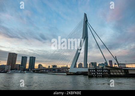 Erasmusbrug oder die Erasmus-Brücke, wie sie am 20. Januar 2020 in einer magischen Stunde am Winterabend mit buntem Himmel im Stadtzentrum der niederländischen Stadt Rotterdam, Niederlande, zu sehen ist. Die 802m. Lange Brücke über das Wasser der Neuen Maas ist eine von Ben van Berkel entworfene, nach Desiderius Erasmus benannte Brücke mit Kabelgestellen und Bascule. Die Konstruktion und die Struktur sind berühmt für ihre moderne Architektur und das asymmetrische, blassblaue Pylondesign, das auch die größte Platte seiner Art in der Welt hat. Die Brücke ist ein Wahrzeichen, Denkmal für Rotterdam und die Niederlande. (Foto von Nicolas Economou/NurP Stockfoto