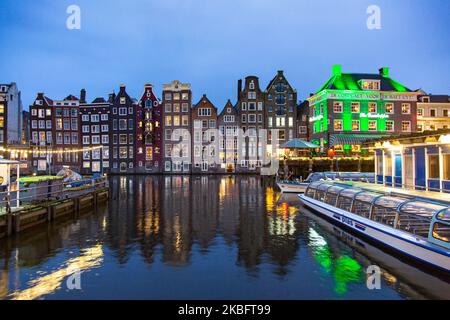 Die berühmten bunten Tanzhäuser mit authentischer holländischer Architektur säumen traditionelle Gebäude mit Lichtern. Die beleuchteten Häuser über dem Wasser am Damrak-Kanal-Becken sind eine berühmte Touristenattraktion, ein Wahrzeichen in der Nähe des Hauptbahnhofs, eine wichtige Touristenattraktion, in Amsterdam, Holland, den Niederlanden, wie sie nach Sonnenuntergang, während der magischen blauen Stunde, Dämmerung und Nacht gesehen werden. Amsterdam, Niederlande (Foto von Nicolas Economou/NurPhoto) Stockfoto