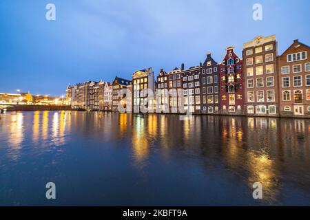 Die berühmten bunten Tanzhäuser mit authentischer holländischer Architektur säumen traditionelle Gebäude mit Lichtern. Die beleuchteten Häuser über dem Wasser am Damrak-Kanal-Becken sind eine berühmte Touristenattraktion, ein Wahrzeichen in der Nähe des Hauptbahnhofs, eine wichtige Touristenattraktion, in Amsterdam, Holland, den Niederlanden, wie sie nach Sonnenuntergang, während der magischen blauen Stunde, Dämmerung und Nacht gesehen werden. Amsterdam, Niederlande (Foto von Nicolas Economou/NurPhoto) Stockfoto