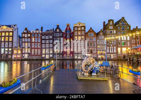 Die berühmten bunten Tanzhäuser mit authentischer holländischer Architektur säumen traditionelle Gebäude mit Lichtern. Die beleuchteten Häuser über dem Wasser am Damrak-Kanal-Becken sind eine berühmte Touristenattraktion, ein Wahrzeichen in der Nähe des Hauptbahnhofs, eine wichtige Touristenattraktion, in Amsterdam, Holland, den Niederlanden, wie sie nach Sonnenuntergang, während der magischen blauen Stunde, Dämmerung und Nacht gesehen werden. Amsterdam, Niederlande (Foto von Nicolas Economou/NurPhoto) Stockfoto