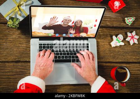 weihnachtsmann mit weihnachtsgeschenken, Videoanruf mit glücklichem weißem Paar Stockfoto