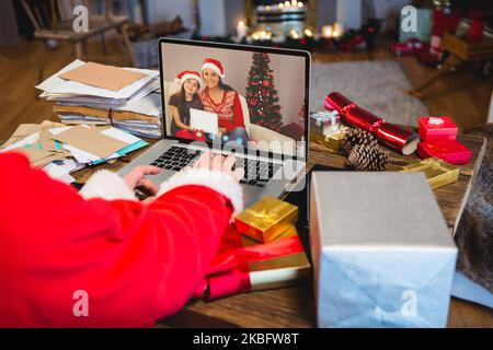 weihnachtsmann mit weihnachtsgeschenken, Videoanruf mit glücklicher, weißer Familie Stockfoto