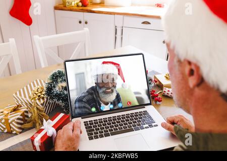 Ein weißer Mann mit weihnachtsmannmütze, der ein Videogespräch mit einem glücklichen afroamerikanischen Mann führt Stockfoto