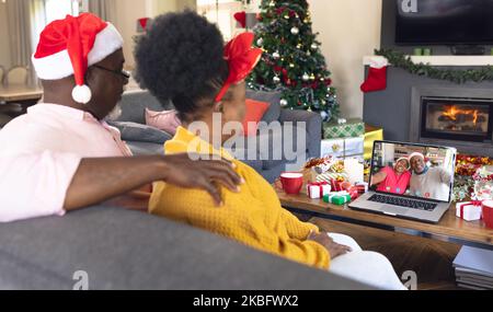 Ein afroamerikanisches Paar mit weihnachtsmannmützen, das Videoanrufe mit einem glücklichen afroamerikanischen Paar führt Stockfoto