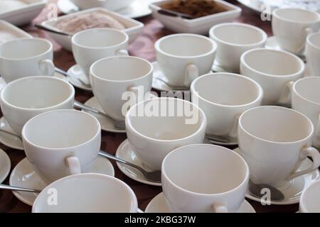 Viele weiße Kaffeetassen in einer Reihe über einem Buffet Stockfoto