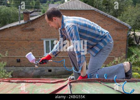 Dachdecker Bauarbeiter mit Pulverisierer Sprühen Farbe auf Metallblechdach Stockfoto