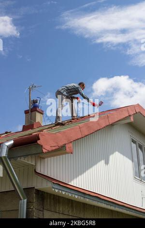 Im Sommer auf dem Dach malt ein Mann das Dach rot Stockfoto