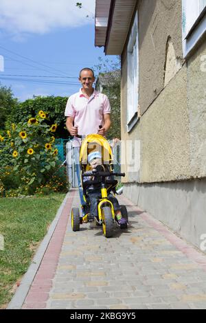 Vater seinen Sohn, ein Dreirad auf dem Bürgersteig zu fahren Stockfoto