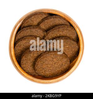 Kreisförmige Pumpernickel-Scheiben, in einer Holzschale. Ein schweres, leicht süßes und dunkelbraunes Roggenbrot, das traditionell aus grob gemahlenem Roggen hergestellt wird. Stockfoto