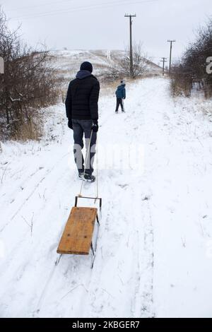 Ein Mann zieht den Schlitten im Schnee am Rücken zum Berg Stockfoto