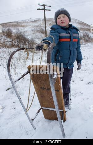 Im Winter steht der Junge und hält den Schlitten im Stehen Stockfoto