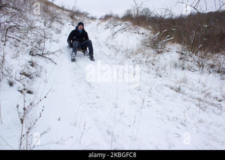 Im Winter geht der Typ auf einem Schlitten den Berg hinunter Stockfoto