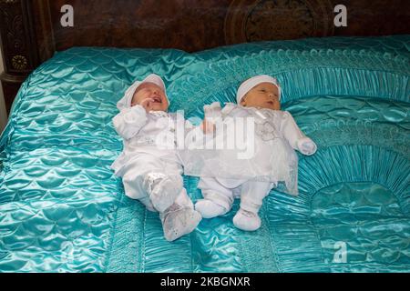 Kleine Mädchen- und Jungzwillinge sind auf dem großen Bett in Weiß gekleidet Stockfoto