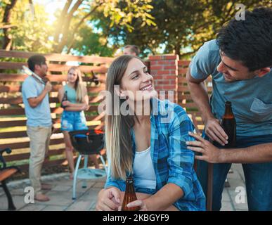 Ein junger Mann und eine junge Frau, die Bier trinken und mit Freunden beim Grillen flirten. Stockfoto