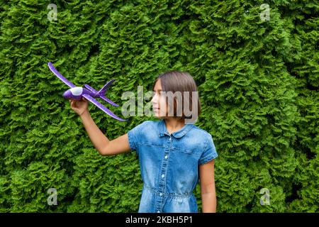 Ein Mädchen hält im Sommer im Park vor dem Hintergrund grüner Bäume ein Spielzeugflugzeug in den Händen. Stockfoto