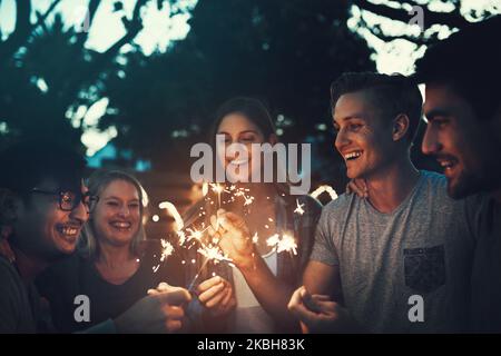 Unvergessliche Momente mit der Mannschaft. Eine Gruppe fröhlicher junger Freunde, die sich am Abend mit Wunderkerzen gemeinsam draußen amüsieren. Stockfoto