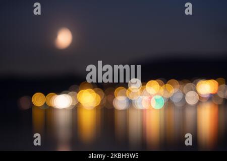 Bunte künstlerische Lichter einer Stadt auf dem See zusammen mit dem Mond in der Nacht Stockfoto