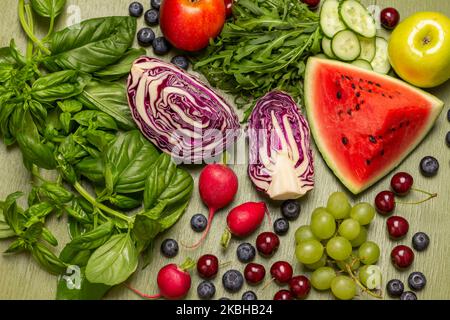 Mischung aus frischem Gemüse, Obst, Beeren und Gemüse. Zweige aus grünem Basilikum und Rucola. Flach liegend. Grüner Hintergrund Stockfoto