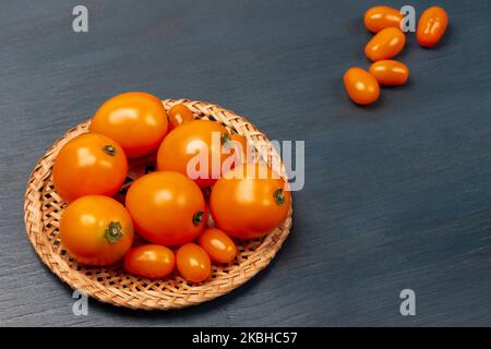 Ganze gelbe Tomaten auf einem Korbteller und auf dem Tisch. Speicherplatz kopieren. Draufsicht. Blauer Hintergrund. Stockfoto