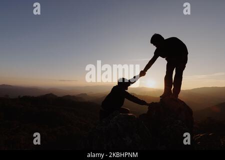 Silhouetten von zwei Menschen, die auf den Berg klettern und helfen. Hilfe- und Hilfekonzept. Stockfoto