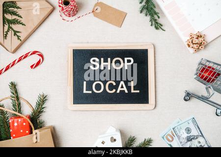Shop lokaler Text auf Tafel geschrieben. Flat Lay mit Support Local Business Quote, Weihnachtsdekoration und Einkaufstasche, Geschenkboxen und Personal Stockfoto
