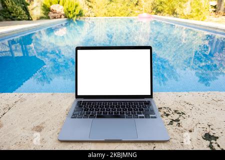 Laptop-Modell, weißer leerer Bildschirm mit modernem Notebook-Modell. Wunderschönes Haus Schwimmbad Hintergrund im Wald. Sonniger Sommertag. Urlaubstechnik. Stockfoto