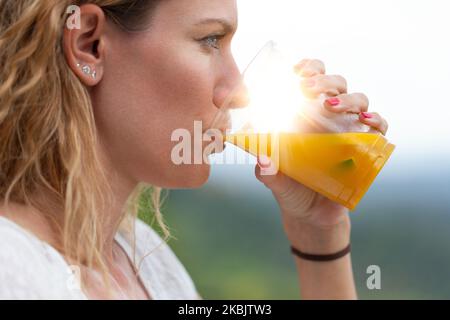 Junge Frau mit lockigen Haaren, die bei Sonnenaufgang frischen Saft trinkt, Nahaufnahme, Profilansicht Stockfoto