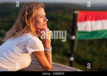 Junge, fröhliche kaukasische Frau, die in die Ferne in der Natur bei der ungarischen Flagge, Ungarn, schaut Stockfoto