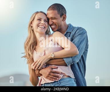 Interracial paar, Lächeln umarmen im Freien und glücklich zusammen für Flitterwochen, Urlaub oder Sommerreise. Schwarzer Mann umarmen, kaukasische Frau mit Comic Stockfoto