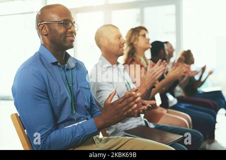 Stolz auf ihre Fortschritte auf dem Weg zum Erfolg. Eine vielfältige Gruppe kreativer Mitarbeiter applaudiert innen. Stockfoto