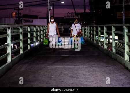 Verkäufer mit Schutzmaske passieren eine Fußgängerüberführung und verlassen den Markt vor der Ausgangssperre in Quezon City, Philippinen, am 20. März 2020. Trotz Warnungen und Richtlinien, die die Ausbreitung von COVID-19 verhindern sollen, strömen einige Menschen immer noch auf den Markt und halten sich nicht an die Empfehlungen zur sozialen Distanzierung. Im Rahmen der "erweiterten Quarantäne" der Gemeinschaft auf der Insel Luzon werden Klassen, Arbeit und Massenverkehr mit einigen Ausnahmen ausgesetzt. (Foto: Lisa Marie David/NurPhoto) Stockfoto