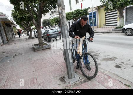 Ein Mann legt in den leeren Straßen der nordtunesischen Stadt Ariana französische Stöcke auf sein Fahrrad, bevor er als weniger als eine halbe Stunde nach Hause fährt, von 6pm bis 6am eine tägliche Ausgangssperre, die vom tunesischen Präsidenten verhängt wurde, Kais Saied, um die Ausbreitung des Coronavirus COVID-19 zu verlangsamen, wird am 18. März 2020 in Tunesien beginnen. (Foto von Chedly Ben Ibrahim/NurPhoto) Stockfoto