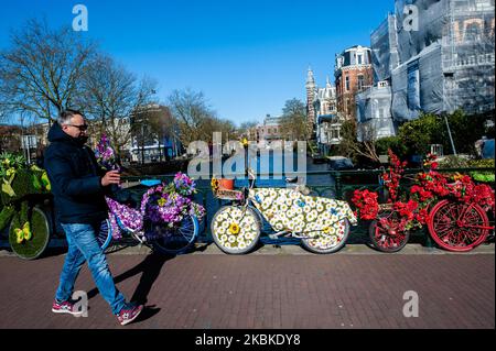 Ein Tourist zeigt in Amsterdam während der Coronavirus-Situation in den Niederlanden am 23.. März 2020 eine Gruppe von mit Blumen geschmückten Fahrrädern durch sein Handy. (Foto von Romy Arroyo Fernandez/NurPhoto) Stockfoto