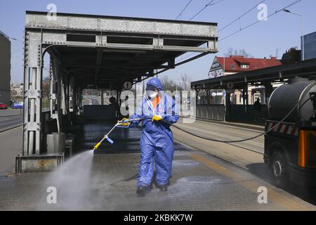 Ein Mitarbeiter der Municipal Cleaning Company (MPO) verwendet einen Druckschlauch, um Bus- und Straßenbahnhaltestellen sowie öffentliche Plätze mit Reinigungsmitteln gegen die Ausbreitung des Coronavirus zu desinfizieren. Krakau, Polen, am 27. März 2020. Die polnische Regierung beschloss, im ganzen Land neue Beschränkungen einzuführen, wie beispielsweise Vorschriften, die das Verlassen der Heimat verhindern, sofern dies nicht gerechtfertigt ist. (Foto von Beata Zawrzel/NurPhoto) Stockfoto