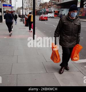 Ein Mann mit Maske trägt am 1. April 2020 Einkaufstaschen der Supermarktkette Sainsbury's entlang der Clapham High Street im Stadtteil Lambeth in London, England. Offizielle Zahlen berichten, dass Lambeth derzeit 418 registrierte Fälle des Covid-19-Coronavirus aufweist, was höher ist als jeder andere Bezirk in London und vierter unter den lokalen Behörden in England insgesamt (hinter Sheffield, Hampshire und Birmingham). Der Bezirk lag zuvor hinter dem benachbarten Stadtteil Southwark im Süden Londons, der mit derzeit 415 Fällen nach wie vor ähnlich hart getroffen ist. (Foto von David Cliff/Nu Stockfoto