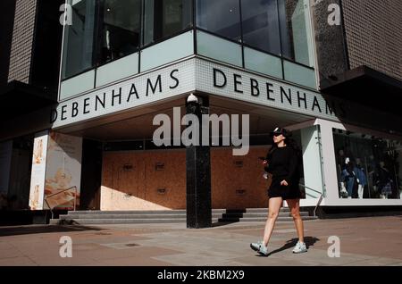 Eine Frau geht am 6. April 2020 an der vernagelten Flagship-Filiale der Kaufhauskette Debenhams in einer fast menschenleeren Oxford Street in London, England, vorbei. Debenhams gab heute bekannt, dass es aufgrund der Schließung aller Filialen im Vereinigten Königreich aufgrund der Sperre des COVID-19-Coronavirus eine Verabreichungsbeschwerde einführen muss. Dies wird das zweite Mal in einem Jahr sein, dass der sich abmühende Einzelhändler die Verwaltung beantragt hat. Die derzeitige Situation kommt nicht lange nach der dauerhaften Schließung von 22 Geschäften, was zu mehr als 700 Arbeitsplatzverlusten führt, wobei weitere 28 bereits für die Schließung geplant sind Stockfoto