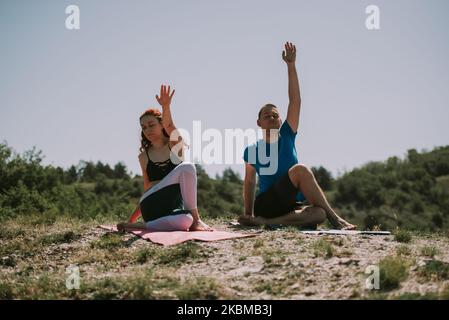 Yoga-Partner machen einige Yoga-Posen, während sie auf der Wiese sitzen Stockfoto