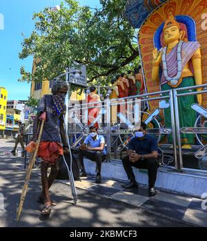 Ein körperlich behinderter, obdachloser Sri-lankischer Mann, der ein Taschentuch trägt, um sein Gesicht zu bedecken, geht als Sri-lankische Männer mit schützenden Gesichtsmasken vor einem buddhistischen Tempel in Colombo, Sri Lanka, auf einen Bus warten. 14. April 2020. Trotz der Anbruch der Singhalesisch und Tamil Neujahr, Sri Lankans haben sich von den Feierlichkeiten zurückgezogen, wie die Polizei Sri Lanka erklärte, dass Feiern für das neue Jahr wurden während der Sperrstunde verboten, wie Ausgangssperre wird auferlegt, um peopleâ €™s Bewegungen in dem Bemühen, die Ausbreitung von COVID-19 enthalten zu beschränken. Nach Angaben des Gesundheitsministeriums von Sri Lanka wurden 7 Todesfälle und 218 positive Todesfälle verzeichnet Stockfoto