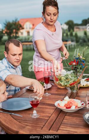 Familie mit einer Mahlzeit vom Grill während des Sommer Picknick im Freien Abendessen in einem Hausgarten. Nahaufnahme von Leuten, die an einem Tisch mit Essen und Geschirr sitzen Stockfoto