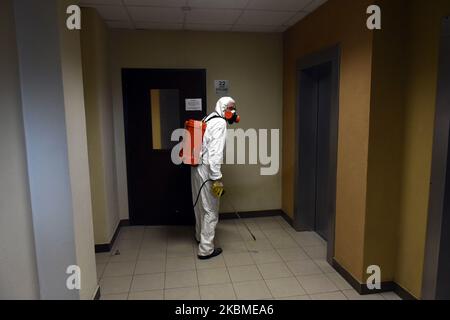 Ein Mitarbeiter der öffentlichen Versorgungsunternehmen, der chemische Schutzkleidung trägt, während er eine Eingangshalle eines Wohnhauses desinfiziert, um die Verbreitung von Covid-19 in Sankt Petersburg, Russland, am 13. April 2020 zu verhindern. (Foto von Sergey Nikolaev/NurPhoto) Stockfoto