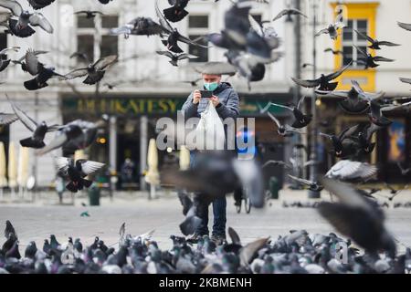 Am 15. April 2020 wird auf dem Hauptplatz in Krakau, Polen, ein Mann mit Gesichtsmaske wegen der Ausbreitung des Coronavirus unter Tauben gesehen. Das Tragen von Gesichtsmasken an öffentlichen Plätzen in Polen ist ab April 16. obligatorisch. (Foto von Beata Zawrzel/NurPhoto) Stockfoto