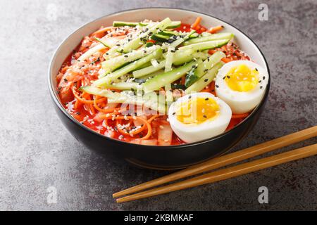 Bibim-guksu Koreanischer würziger Noodles-Salat mit Kimchi, Gurken und Eiern in der Schüssel auf dem Tisch. Horizontal Stockfoto