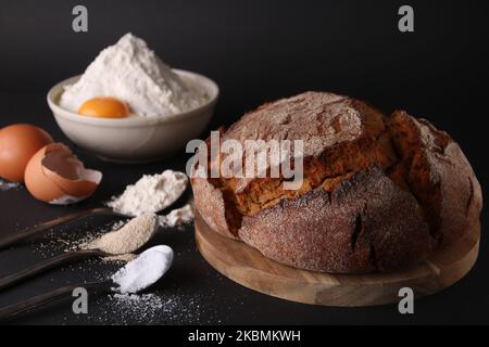 Frisches, rundes Brot auf dem Brett neben den Zutaten für die Zubereitung Stockfoto