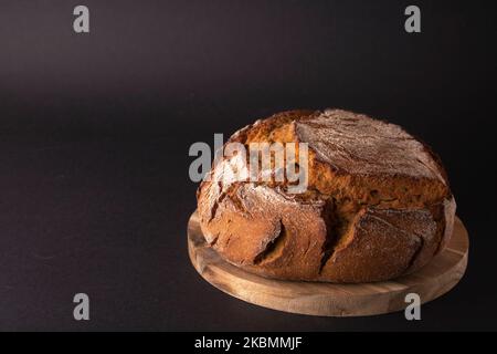 Frisches, rundes Brot liegt in Nahaufnahme auf einem runden Brett auf schwarzem Hintergrund Stockfoto