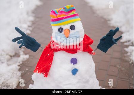 Schneemann in einem Regenbogenhut und einer medizinischen Maske. Stockfoto