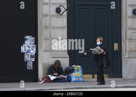 Eine Frau liest ihre Zeitung und geht an die Front einer Obdachlosen, die seine Zeitung in Saint Germain des Pres in Paris liest, als eine Sperre auferlegt wird, um die Rate der Coronavirus-Krankheit (COVID-19) in Frankreich zu verlangsamen, 2. Mai 2020. (Foto von Mehdi Taamallah / NurPhoto) (Foto von Mehdi Taamallah/NurPhoto) Stockfoto